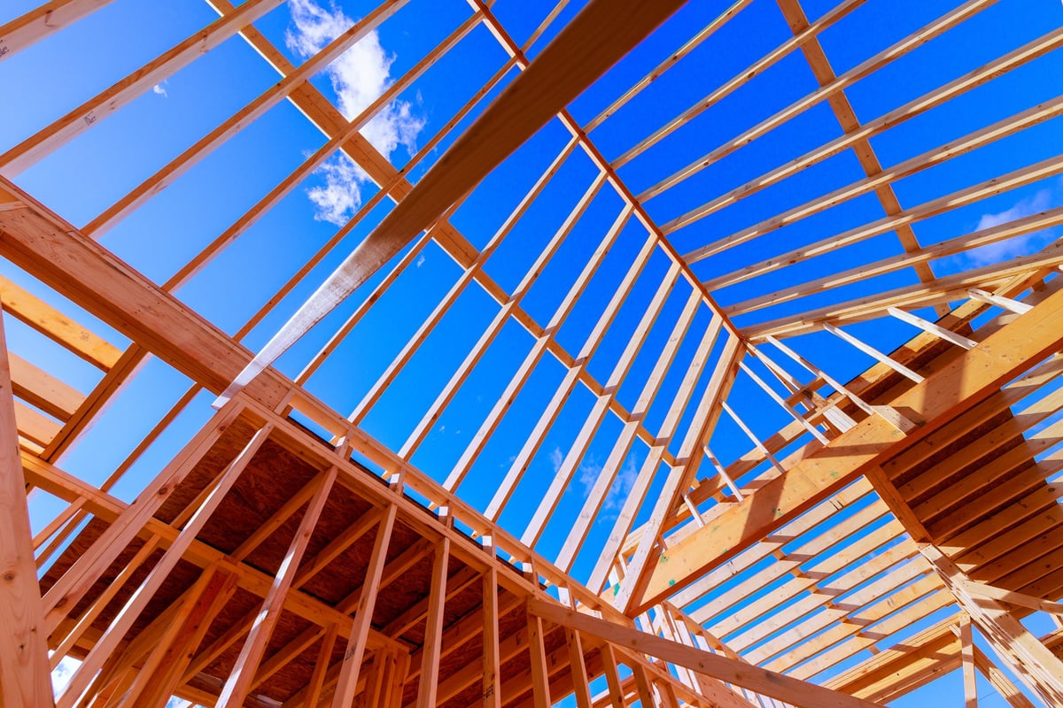 Workers are constructing wooden frame beams for new building under roof trusses.